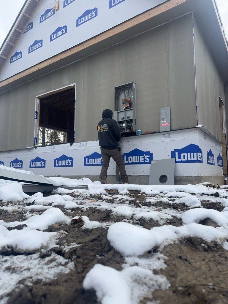 Worker installing siding on a building exterior with snow-covered ground in front