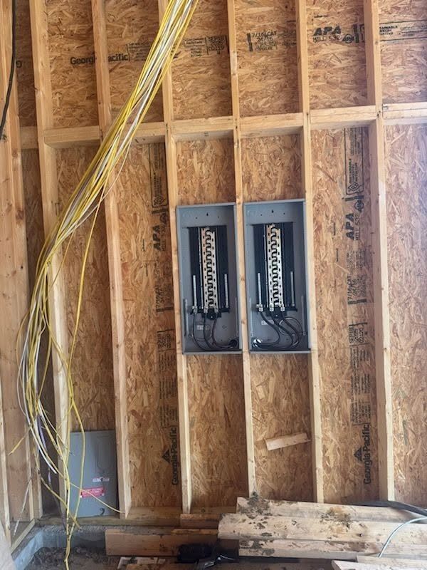 Exposed wall framing with two electrical breaker boxes mounted between studs in a construction area
