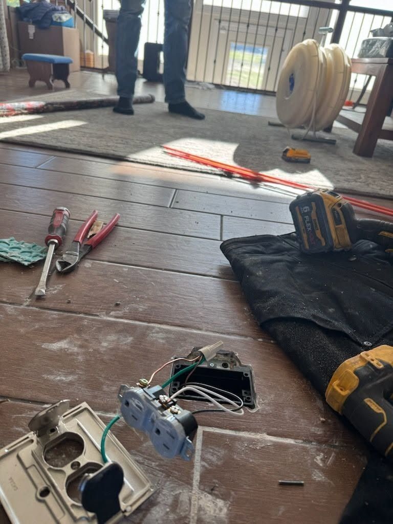 Tools and electrical parts spread on a wooden floor, with a person standing in the background.