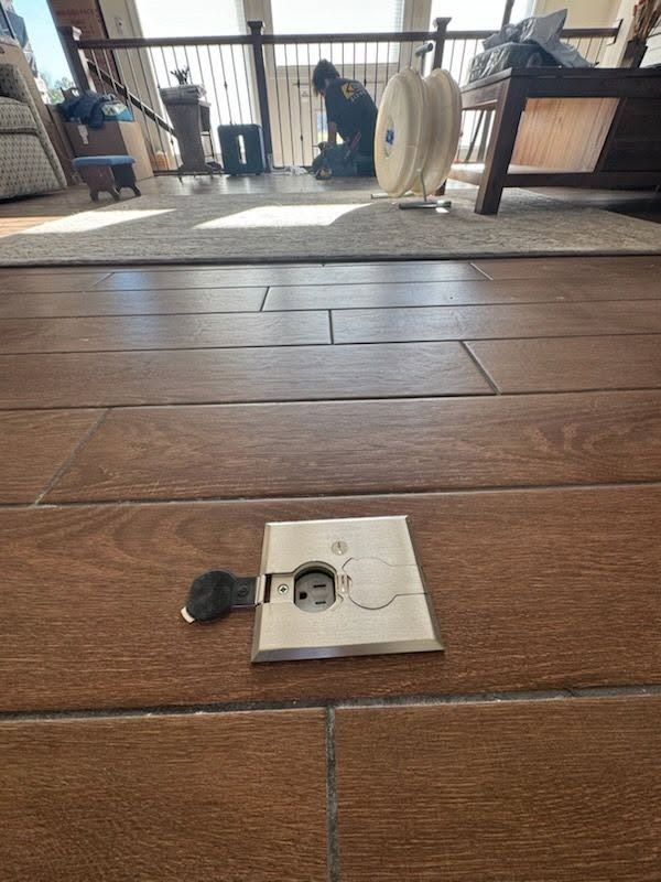 Broken floor outlet plate on a wood floor in a living room