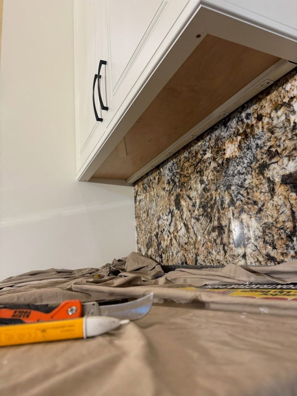 Kitchen countertop demolition with exposed backsplash and tools on a covered counter