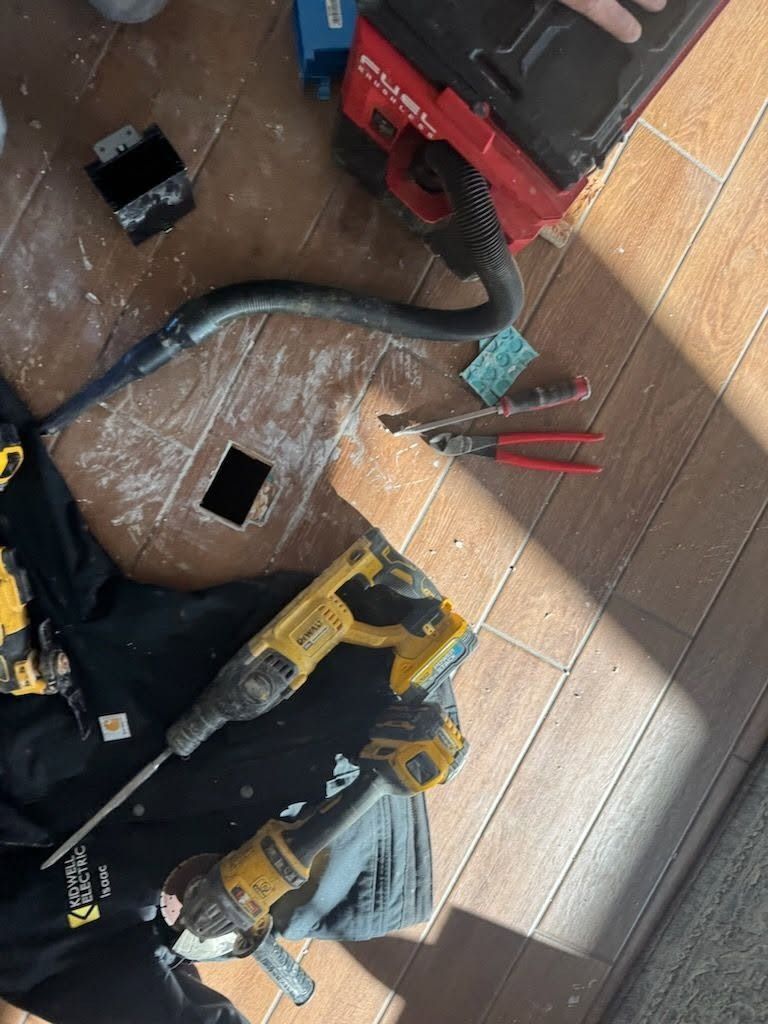 Tools on a tiled floor: red and yellow power tools, cords, and cut cable pieces near a square floor opening.