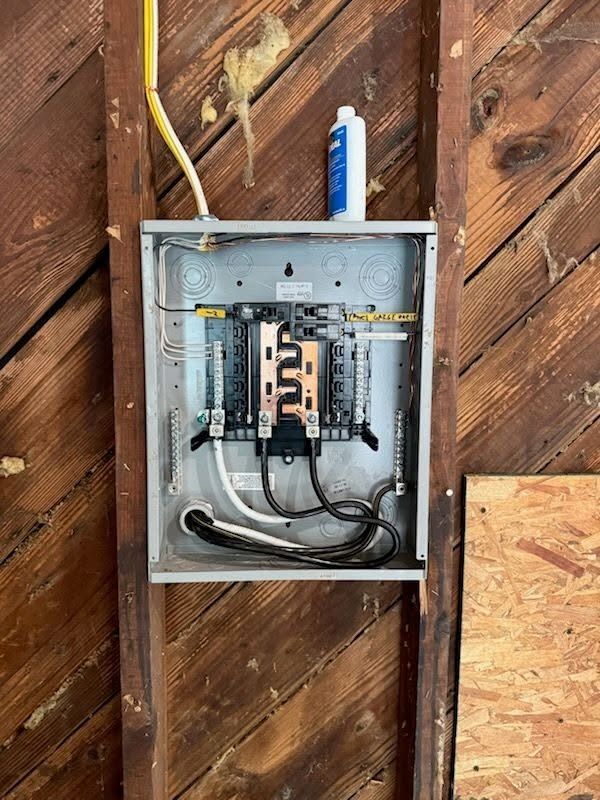 Open electrical breaker panel mounted on a wooden wall with exposed wiring.