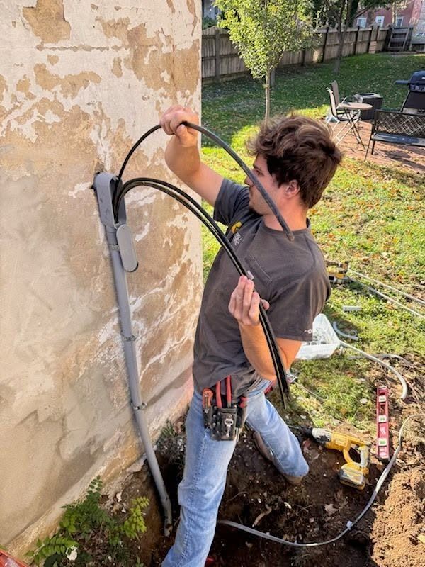 Worker bending beside a house wall, handling cables and tools during exterior utility installation