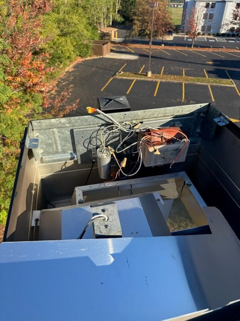 Open rooftop equipment with wires and a metal unit above a parking lot in fall foliage