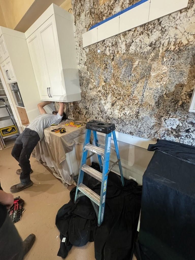 Worker repairing wall with ladder and tools in a room with a large wall mural.