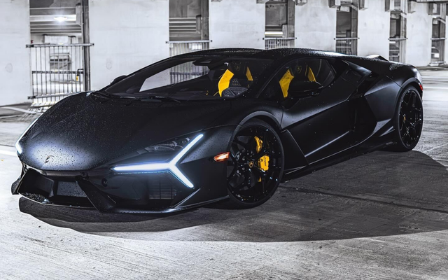 Voiture de sport Lamborghini noire garée à l'intérieur, vue de face en angle avec des accents intérieurs jaunes.