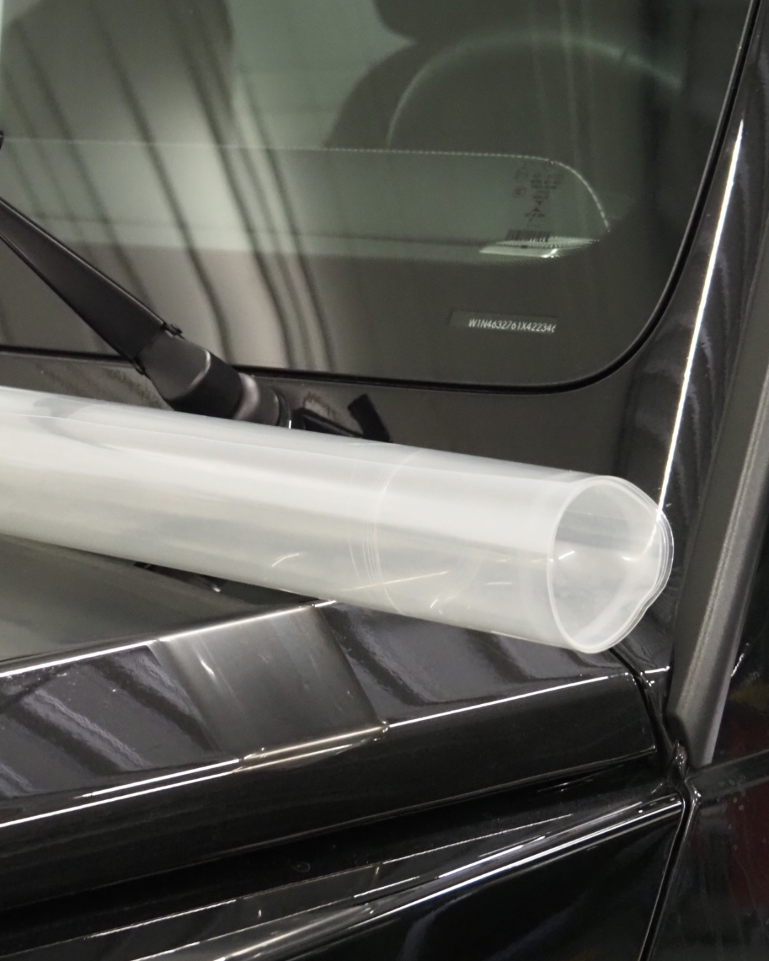 Un tube blanc posé sur le toit d'une voiture noire, près du pare-brise et du rétroviseur latéral.