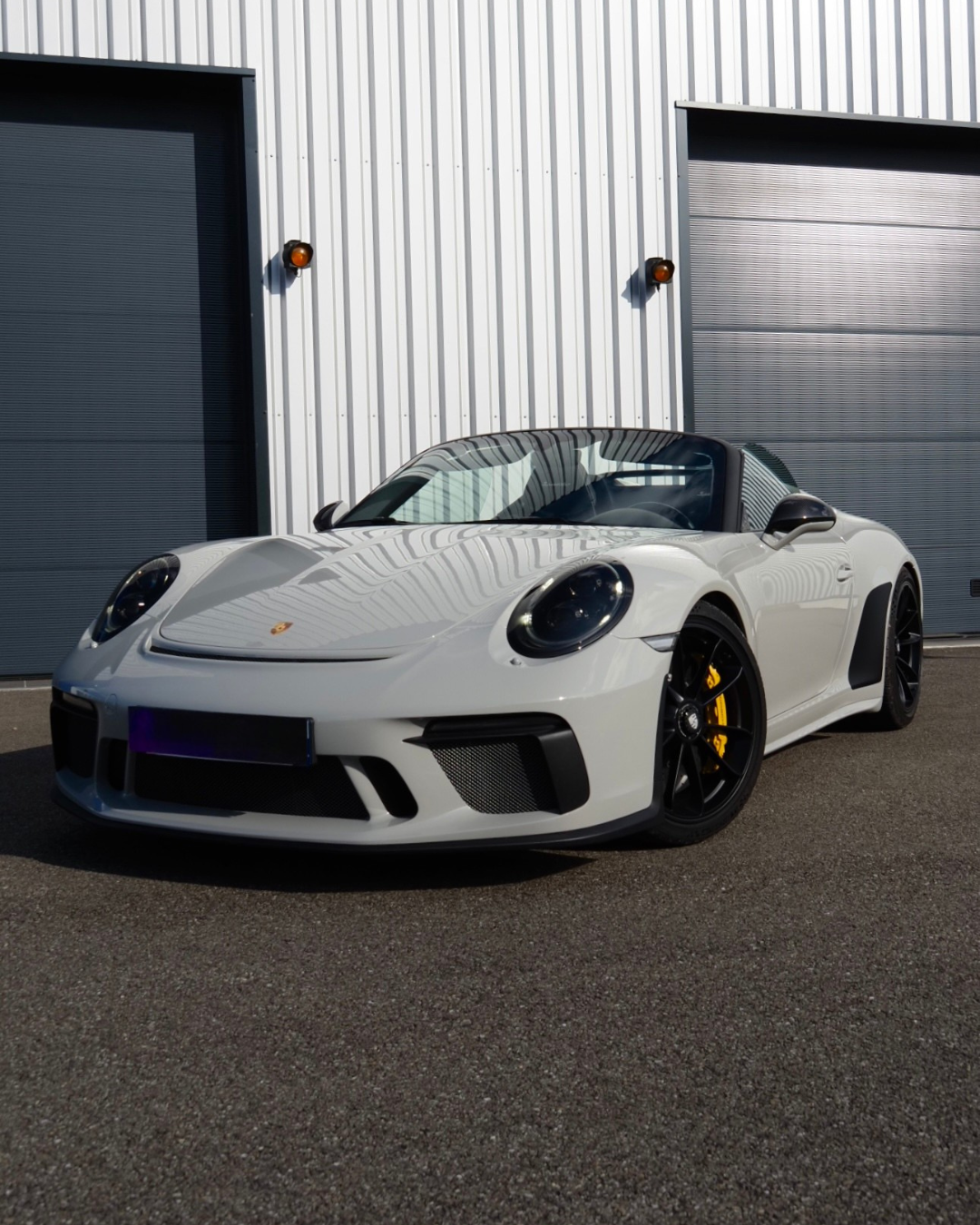 Porsche 911 Cabriolet blanche garée devant des portes de garage industrielles