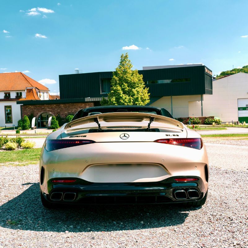 Vue arrière d'une voiture de sport argentée garée dans une rue ensoleillée devant des maisons modernes