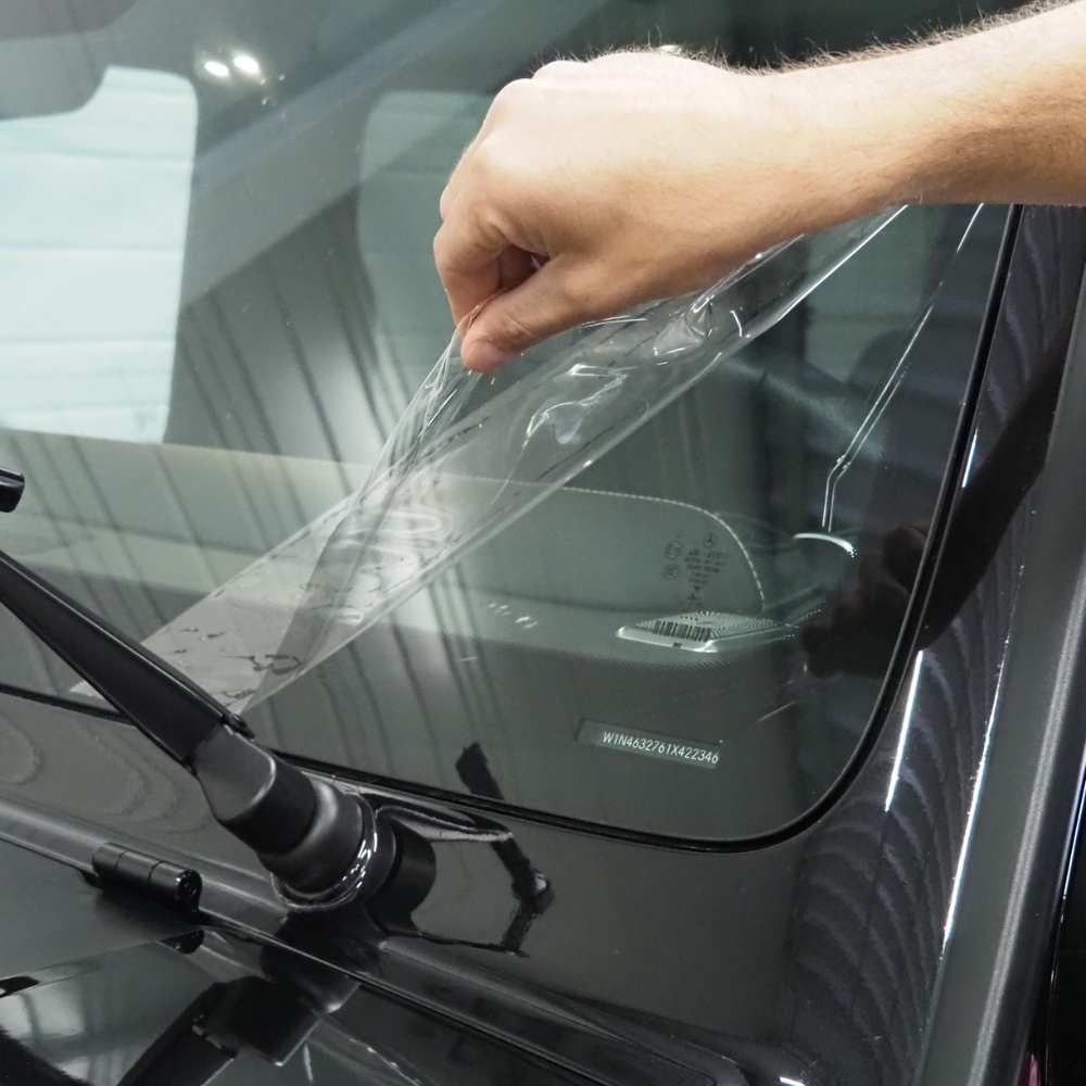 Décollement manuel d'un film protecteur transparent d'un pare-brise de voiture près de l'essuie-glace
