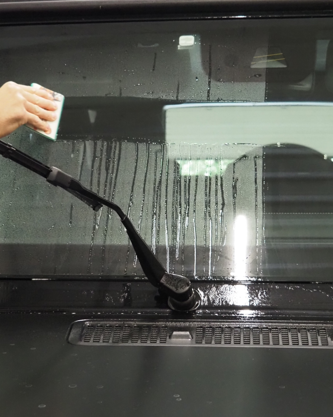 Essuyer manuellement un pare-brise de voiture mouillé avec une raclette près de l'essuie-glace