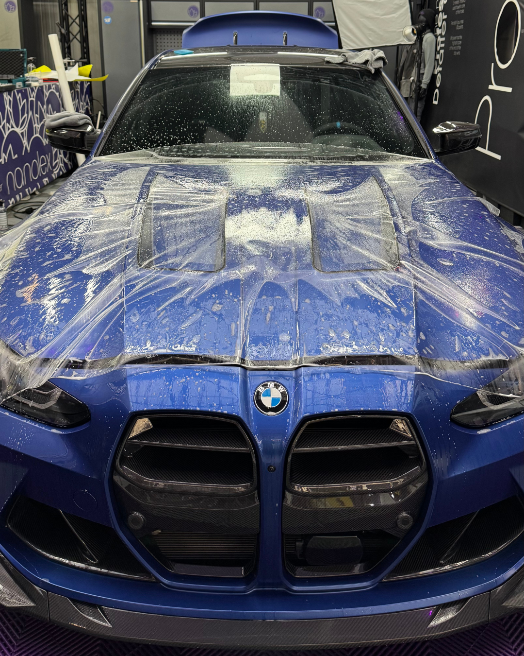 Berline BMW bleue recouverte de mousse de savon lors d'un lavage auto.