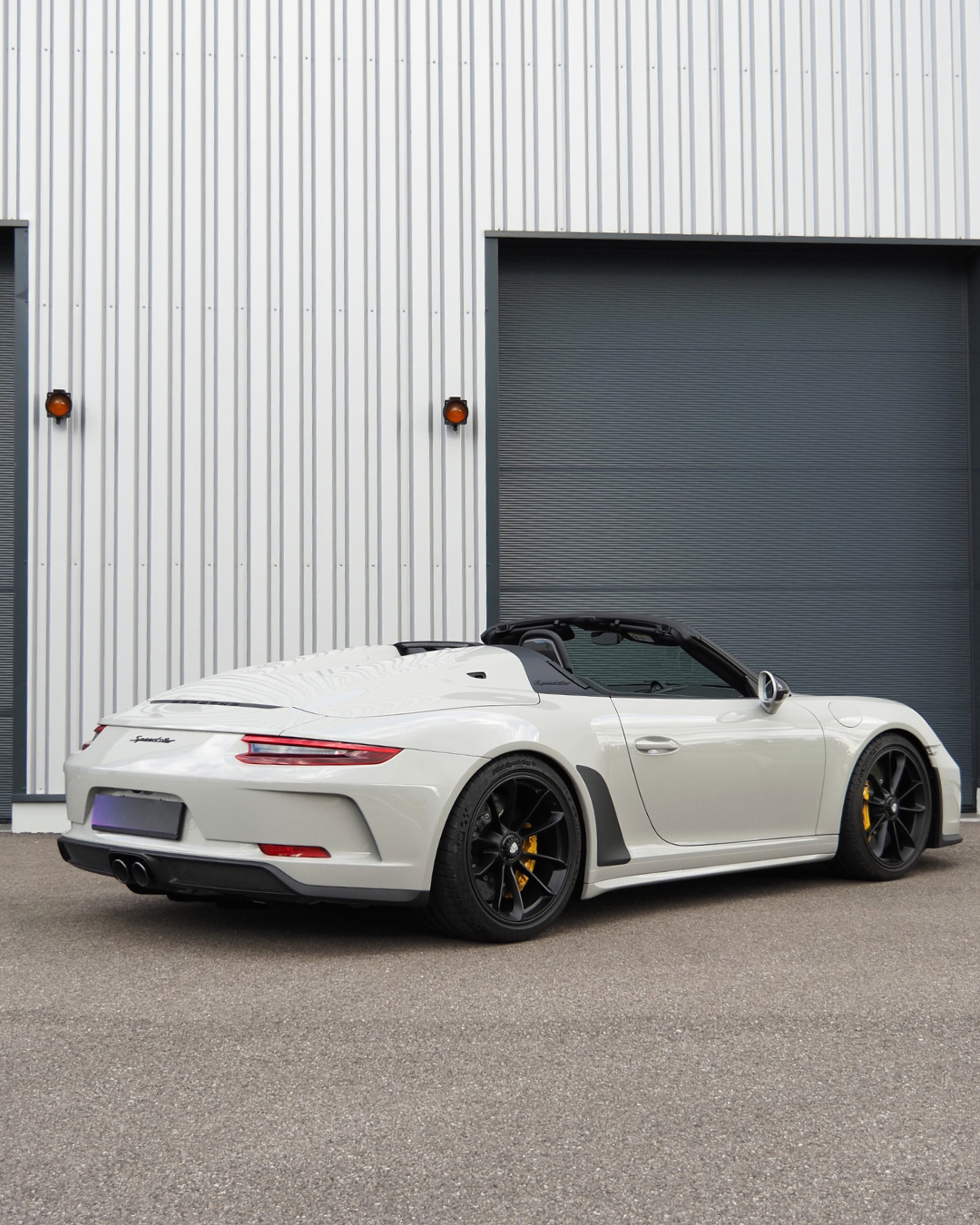Voiture de sport décapotable blanche garée devant un garage industriel gris