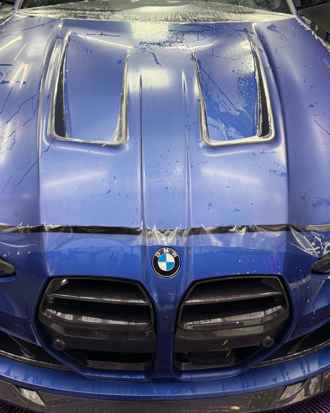 Capot et calandre avant d'une BMW sport bleue, recouverts de gouttelettes d'eau.