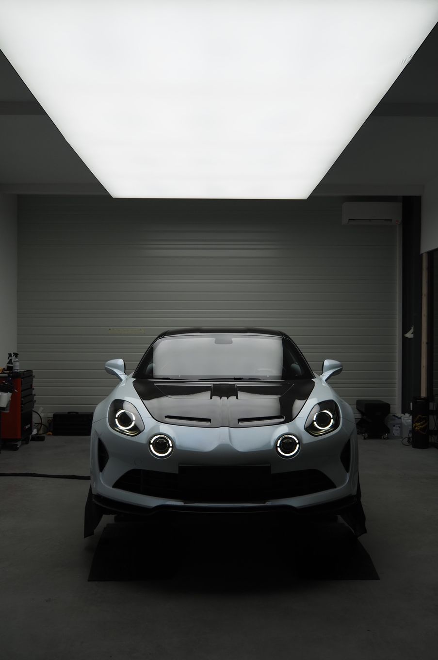 Voiture de sport argentée garée dans un garage sombre sous un plafonnier lumineux.