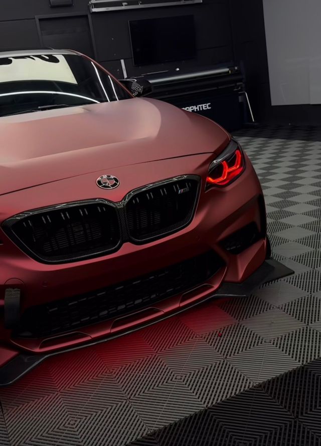 Coupé BMW rouge, phares allumés, dans un garage, vue de l'avant gauche.