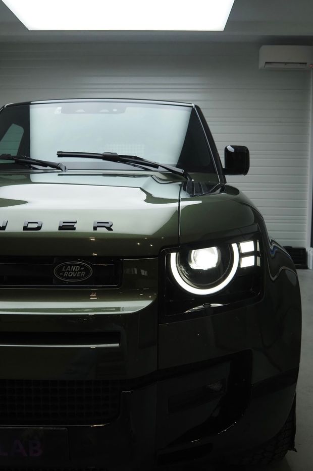 Vue de face d'un Land Rover vert dans un garage, avec un phare allumé.