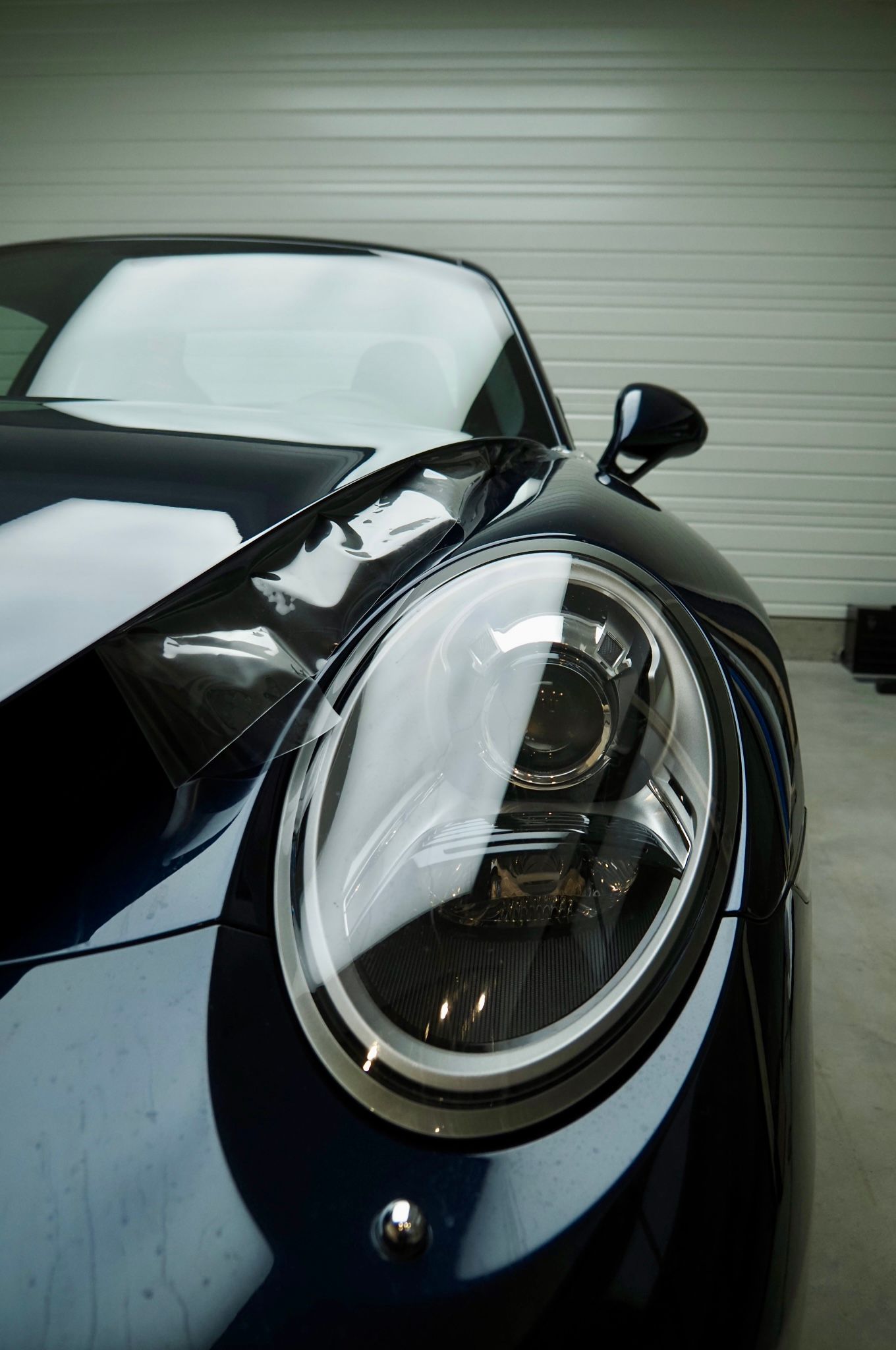 Gros plan sur le phare avant et l'aile d'une voiture de sport noire dans un garage.