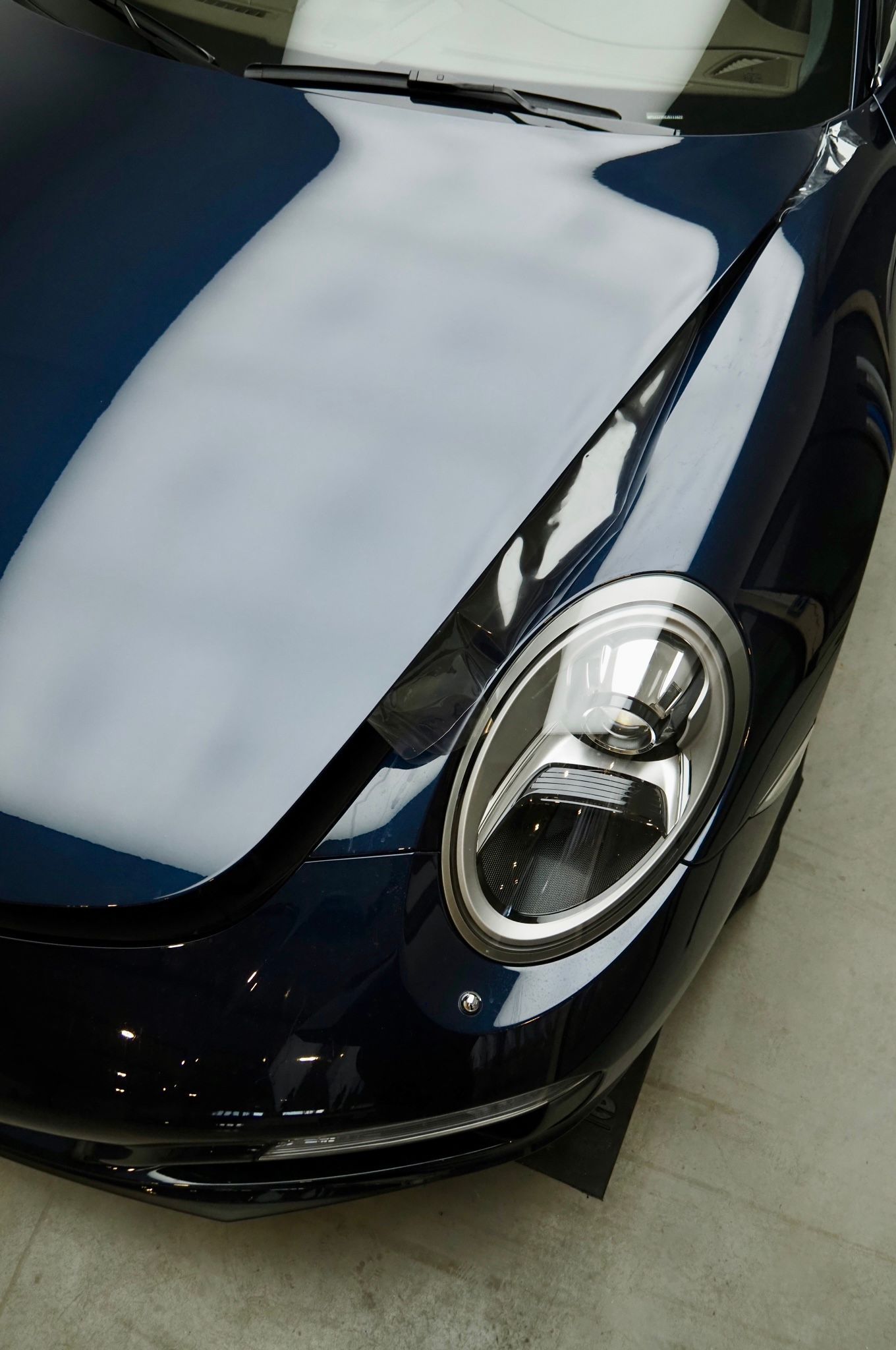 Face avant d'une voiture de sport bleu foncé avec un grand capot et un phare rond, vue de dessus
