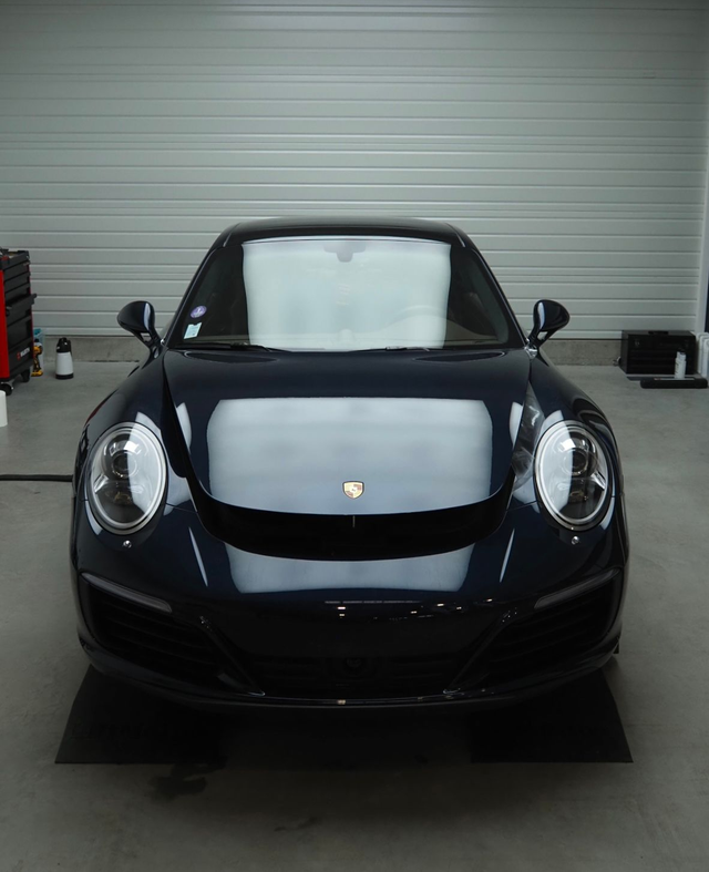Vue de face d'une voiture de sport noire aux phares carénés, dans un garage.