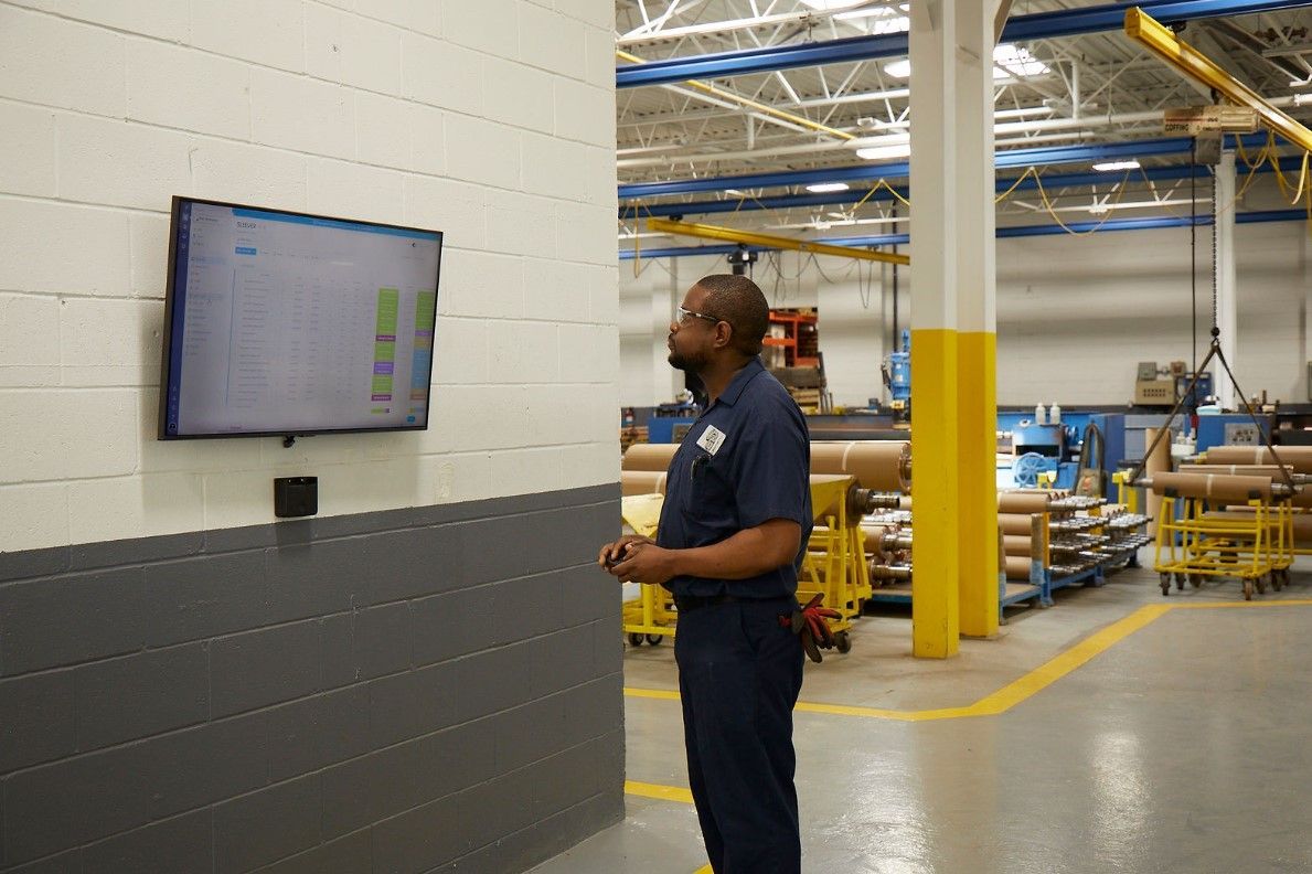A man is standing in a factory looking at a television.
