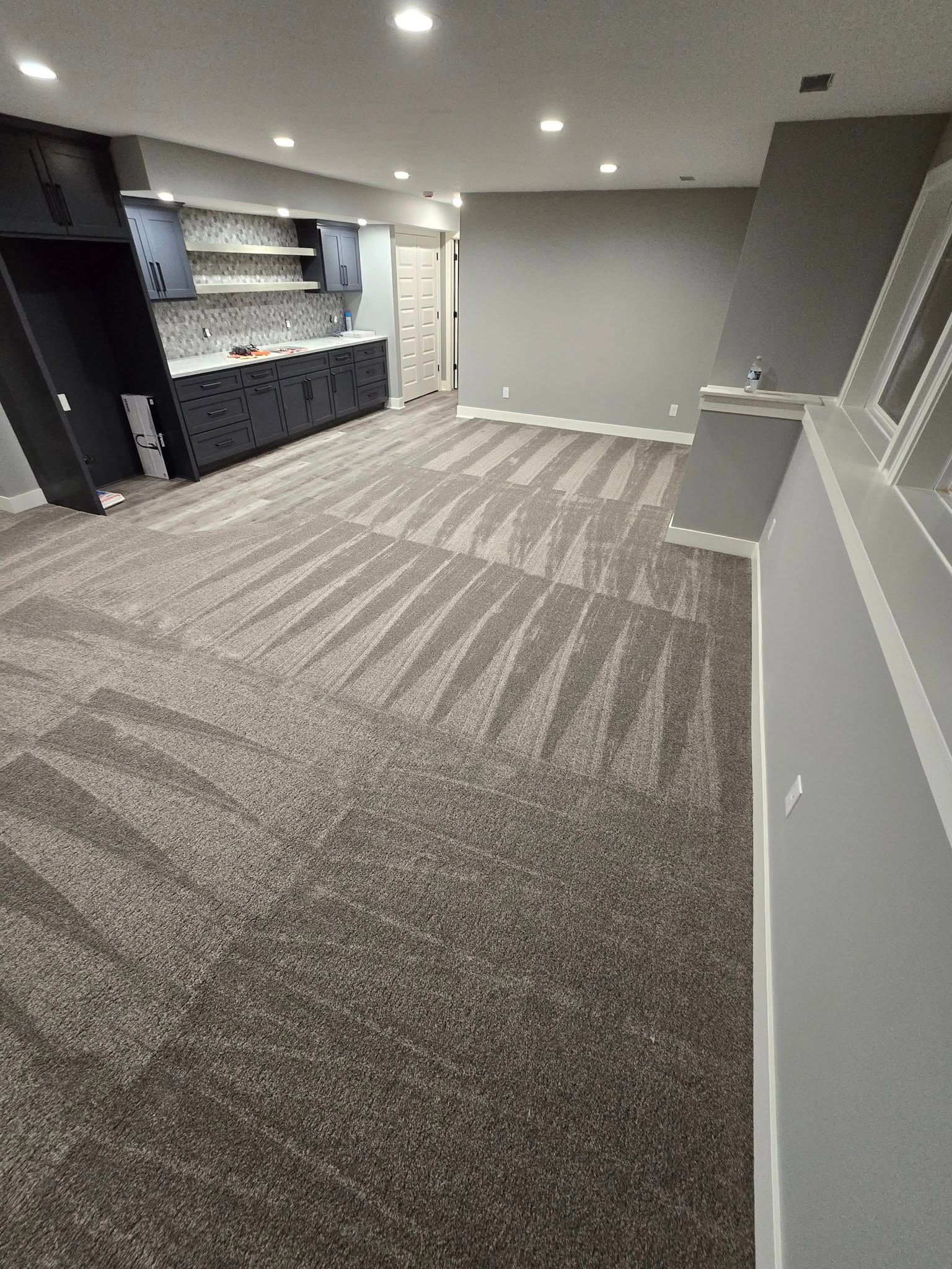 A large room with a carpeted floor and a kitchen in the background.