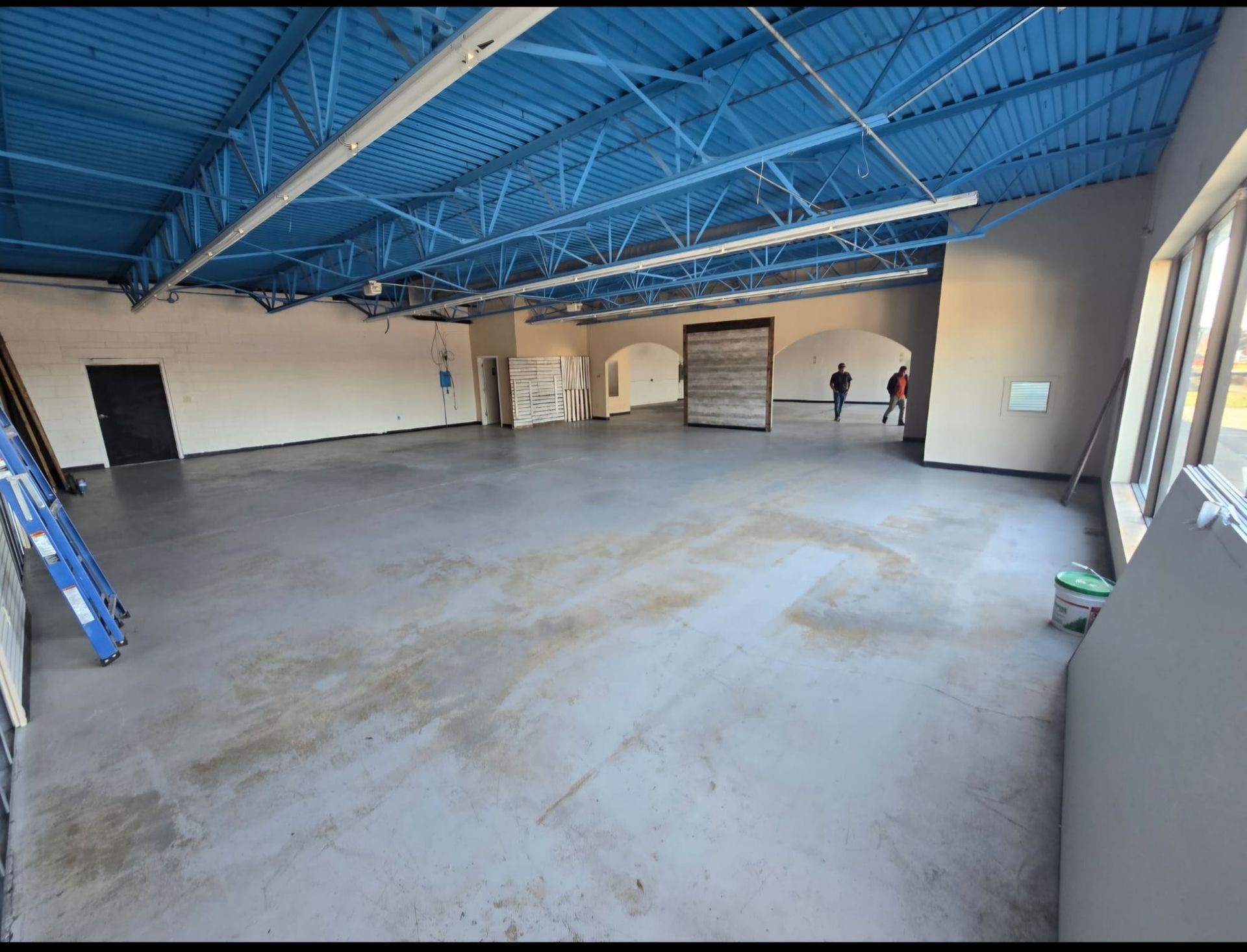 A large empty room with a blue ceiling and a ladder.