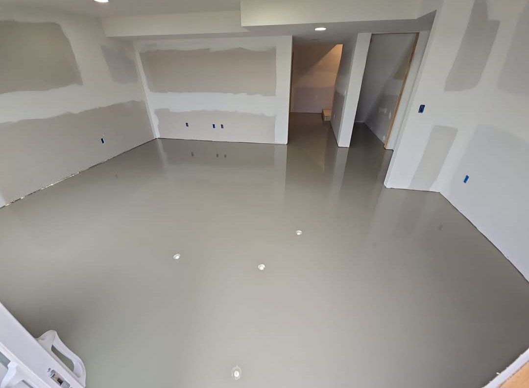 Room with freshly poured, smooth, gray concrete floor; drywall on walls, unfinished.