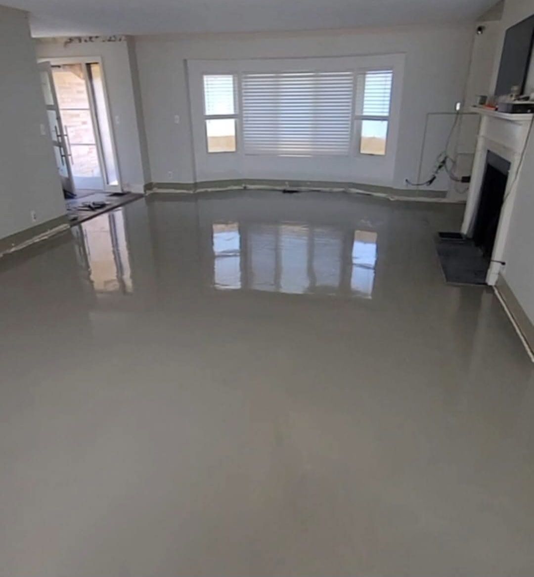 A room with a newly finished, glossy, light gray floor. Windows and a fireplace are visible.