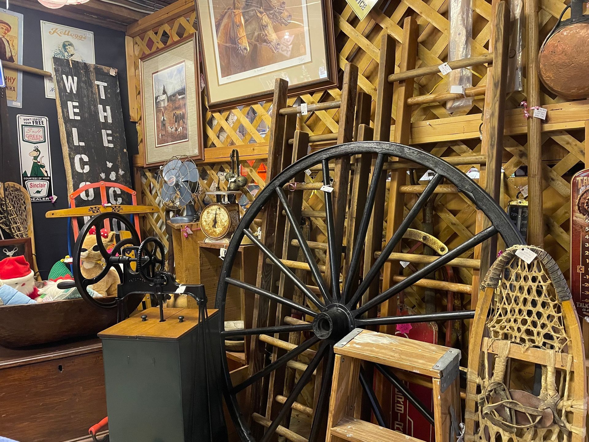 Rustic workshop display with a large wagon wheel, tools, and woven baskets among wooden shelves and decor