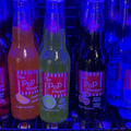 Colorful bottles of soft drinks lined up side by side under blue and purple lighting.