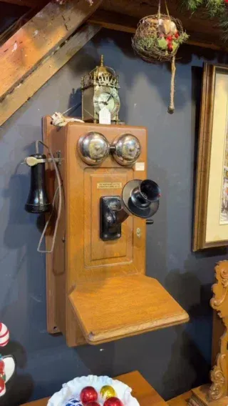 Vintage wall-mounted rotary telephone in a rustic indoor display, with wooden shelf and brass bells.