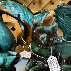 Teal and green glass animal sculptures with price tags on a wooden display shelf