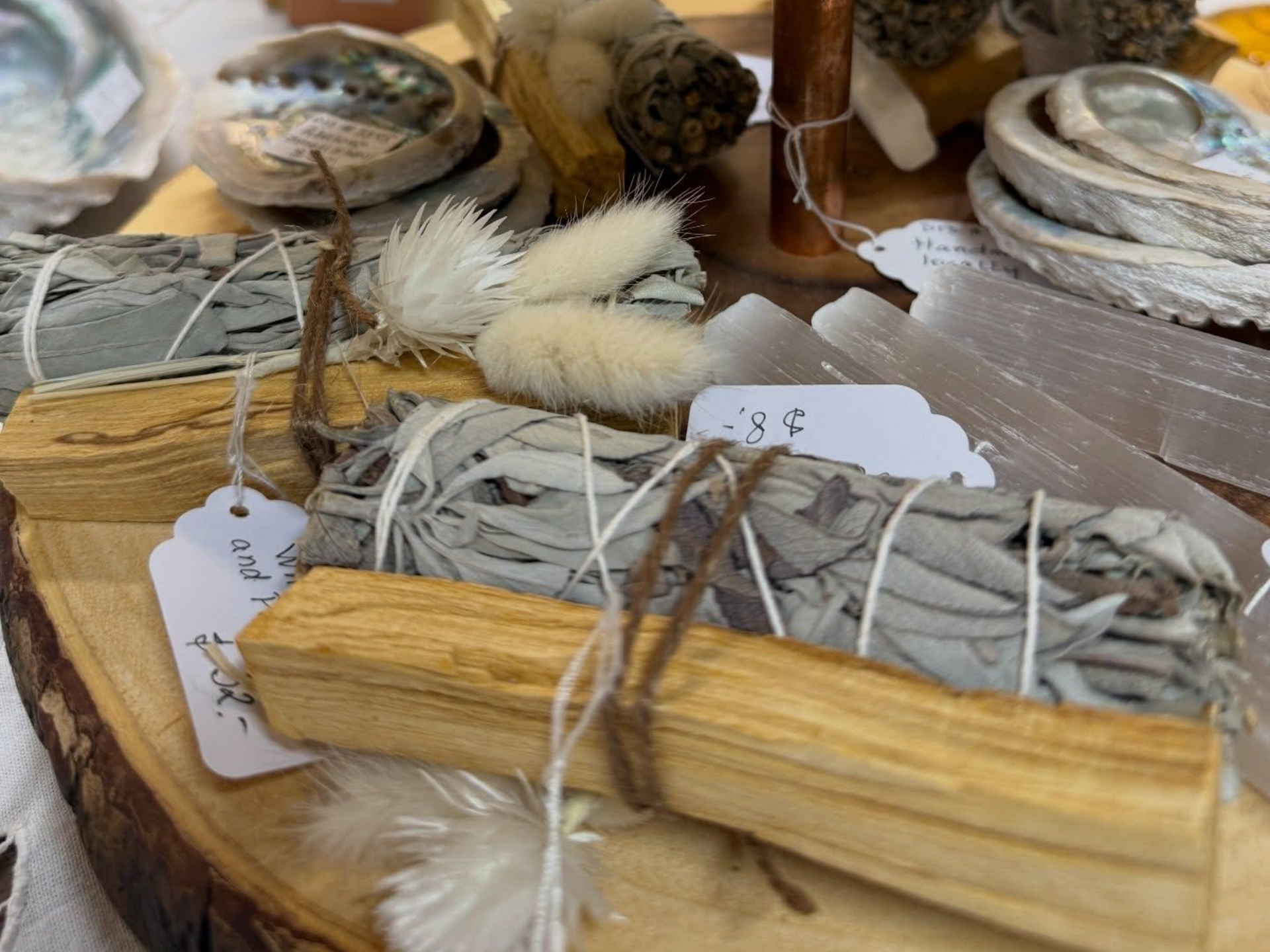 Handmade sage smudge sticks tied with twine and labeled tags on a wooden display table