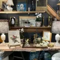 Decorative shelves and a table display with vintage items, bird art, flowers, candles, and lamps in a cozy room
