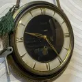 Vintage round wall clock with gold Roman numerals and black center, hanging by a green tassel.