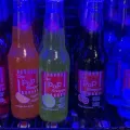 Three colorful Pop Shoppe soda bottles on a shelf under blue lighting