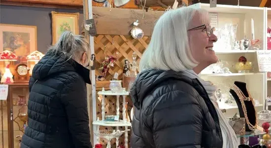 Two people in dark coats browsing displays inside a rustic indoor market shop