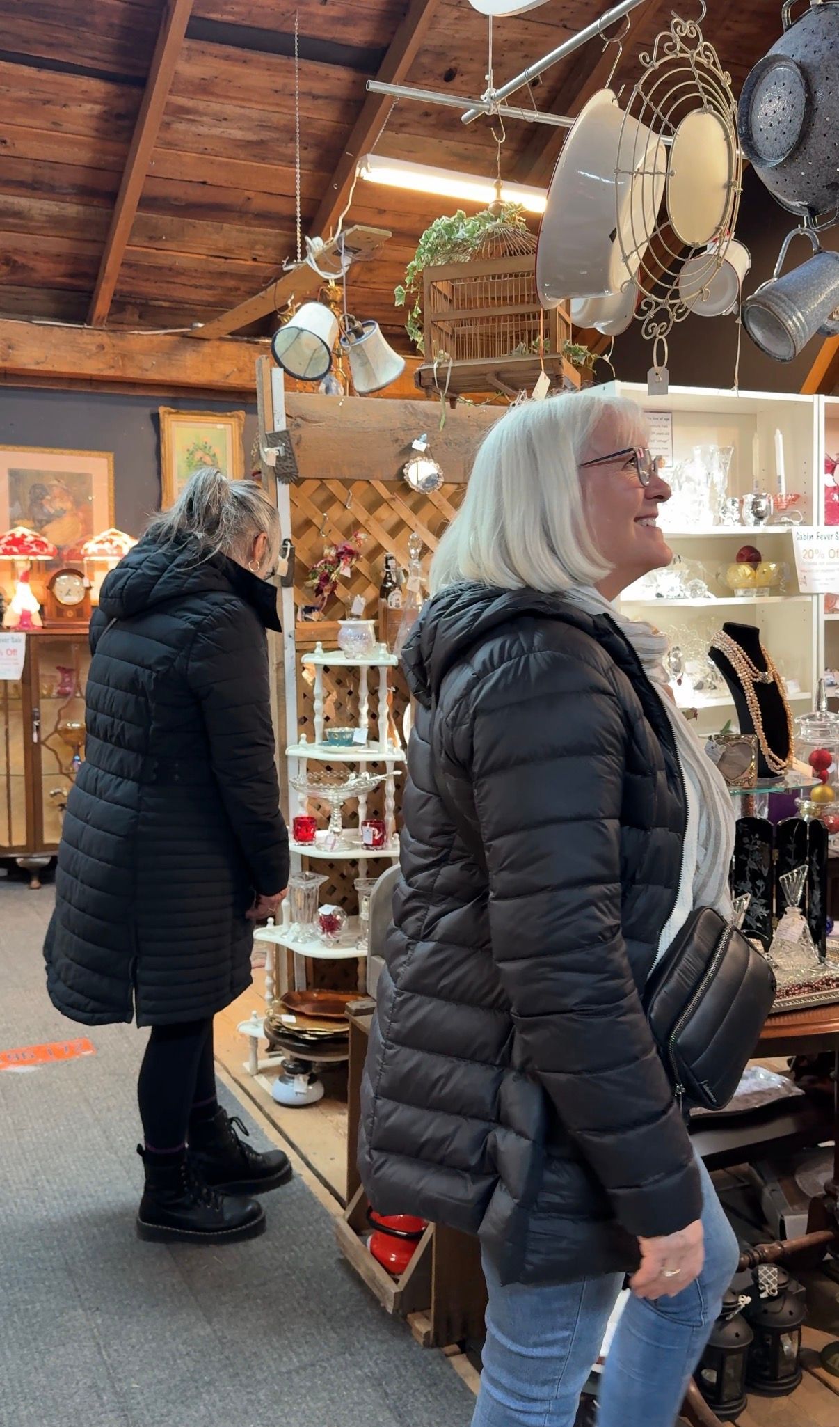 Two people in dark coats browsing displays inside a rustic indoor market shop