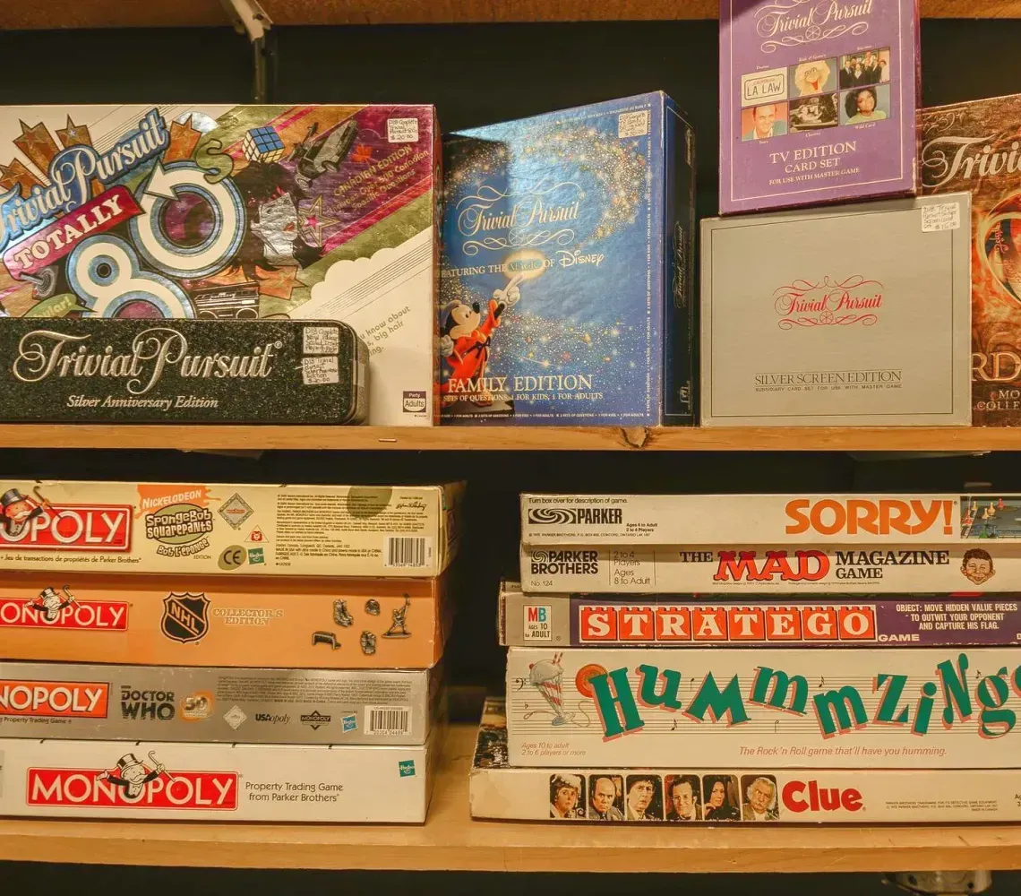 Stacked board games on shelves, including Monopoly, Risk, Clue, and A Game of Thrones.