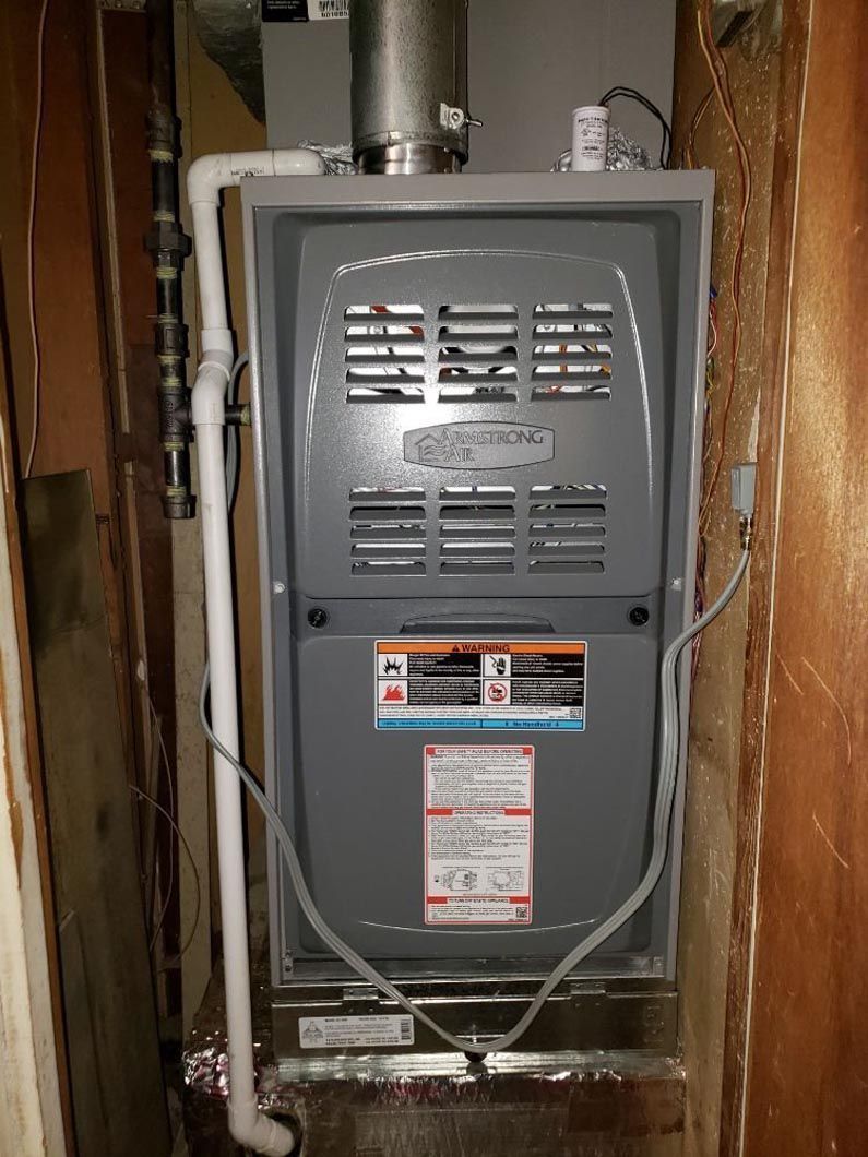 Two outdoor air conditioning units on gravel next to a brown wooden fence.