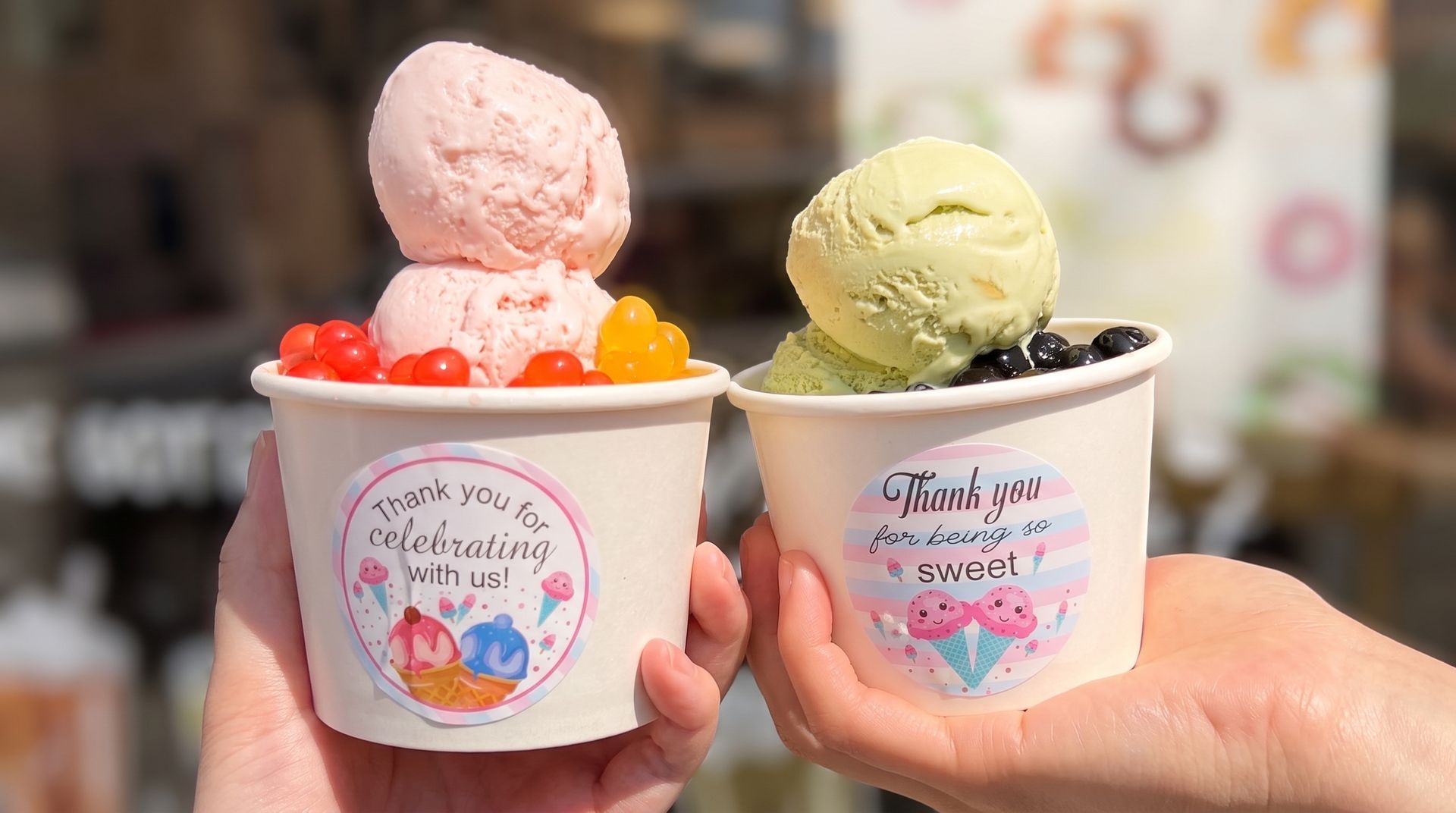 Two pastel ice cream cups held up outdoors, one pink with orange topping and one green