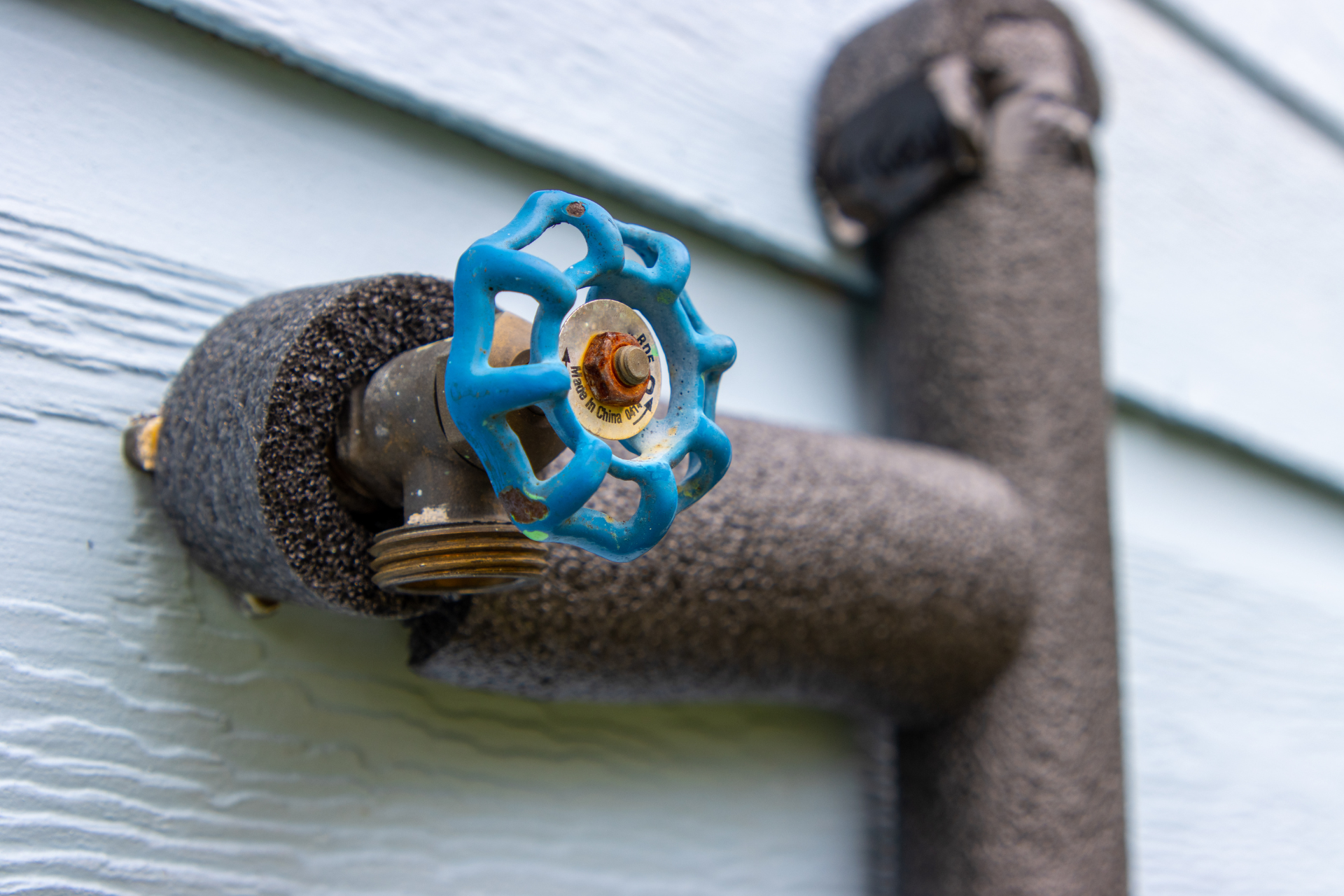 A close up of a faucet with a blue handle on a wall.