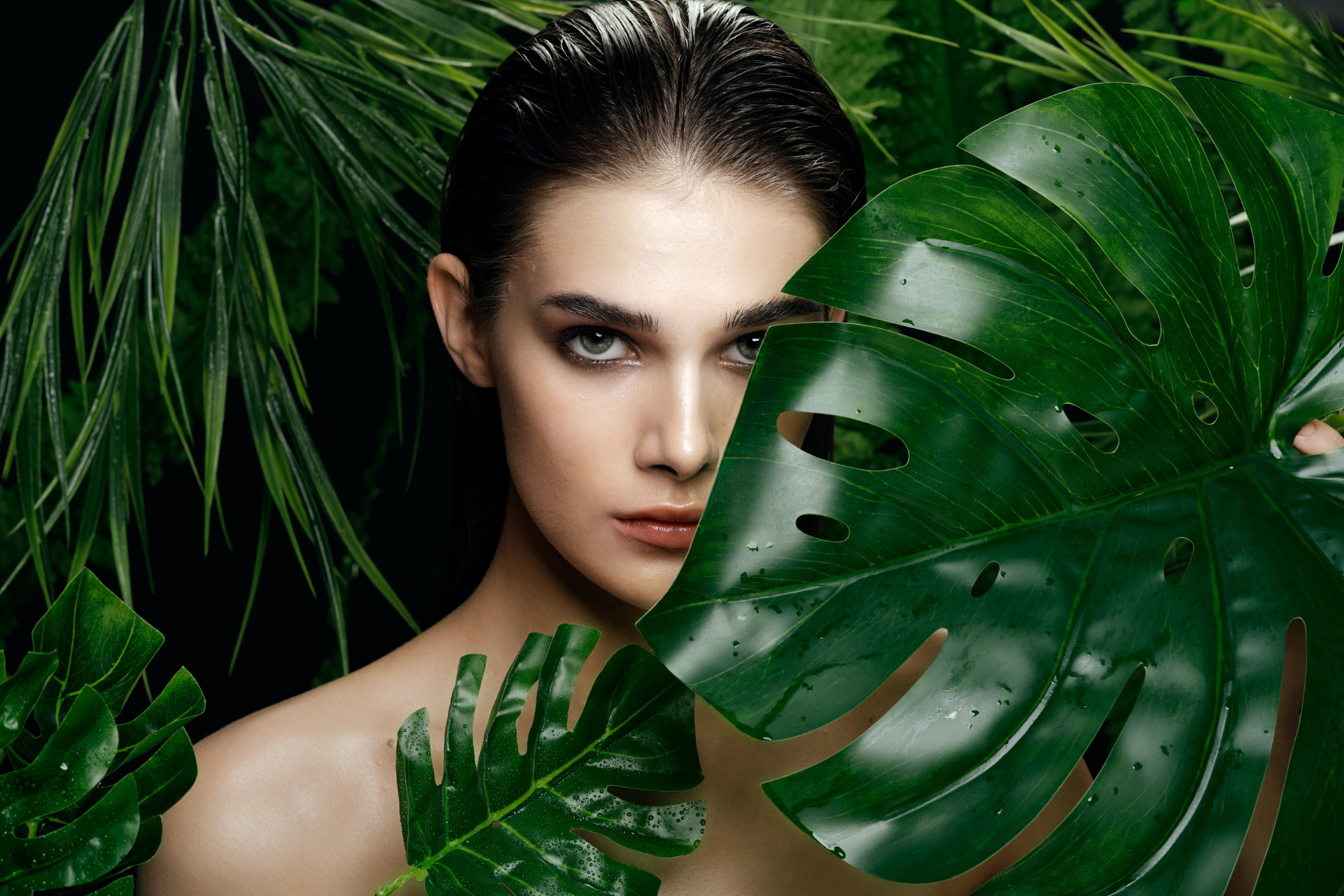 A woman with clear skin framed by green leaves