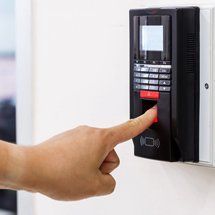 Finger pressing a red-lit keypad on a wall-mounted access control panel
