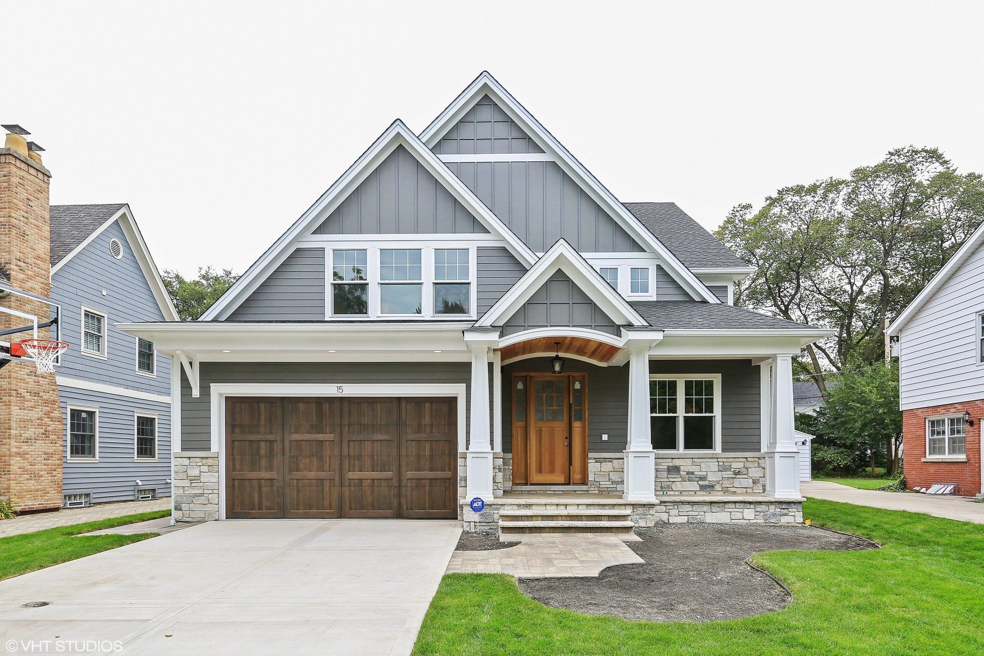 A large gray house with a wooden garage door is for sale.