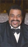Smiling man in a black tuxedo and bow tie against a dark background