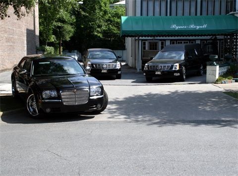 Black sedan parked in front of a building with a green awning, beside two other vehicles.
