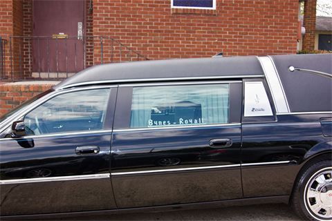 Black hearse parked beside a brick building, side view with tinted windows.